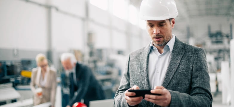 Man wearing suit and white hard hat looking at a cell phone