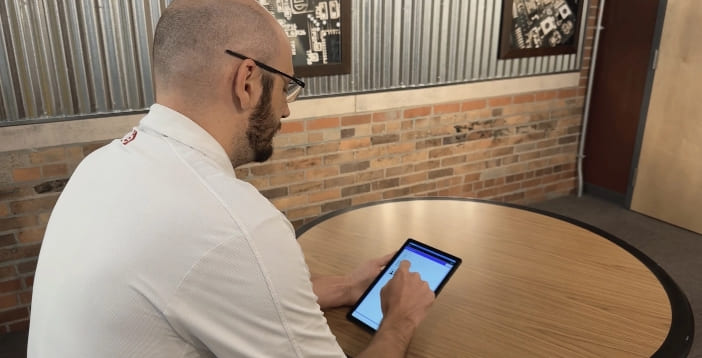 Man with beard and glasses sitting at a table using a tablet