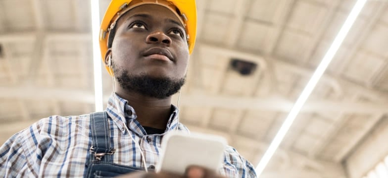 Man wearing yellow hard hat and flannel shirt holding a cell phone