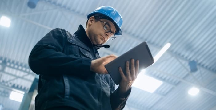 Man wearing blue hard hat and glasses using a tablet